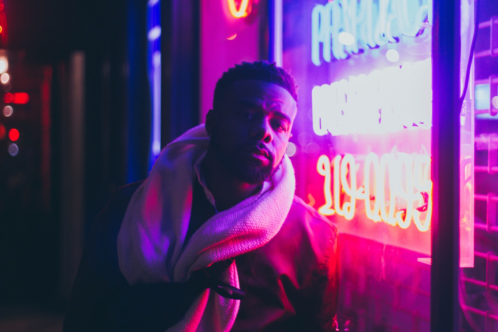 man in red hoodie standing near red and blue neon light signage