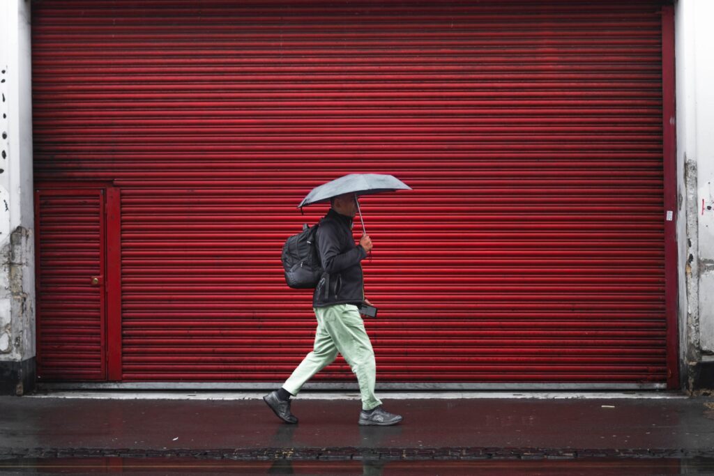 man in black jacket and gray pants holding umbrella walking on sidewalk