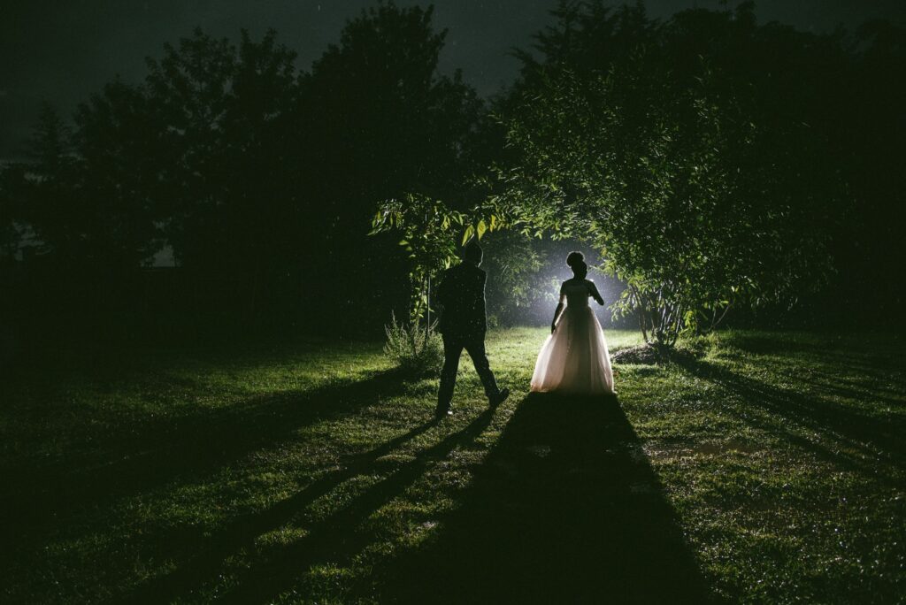 man and woman walking on pathway between trees during nighttime
