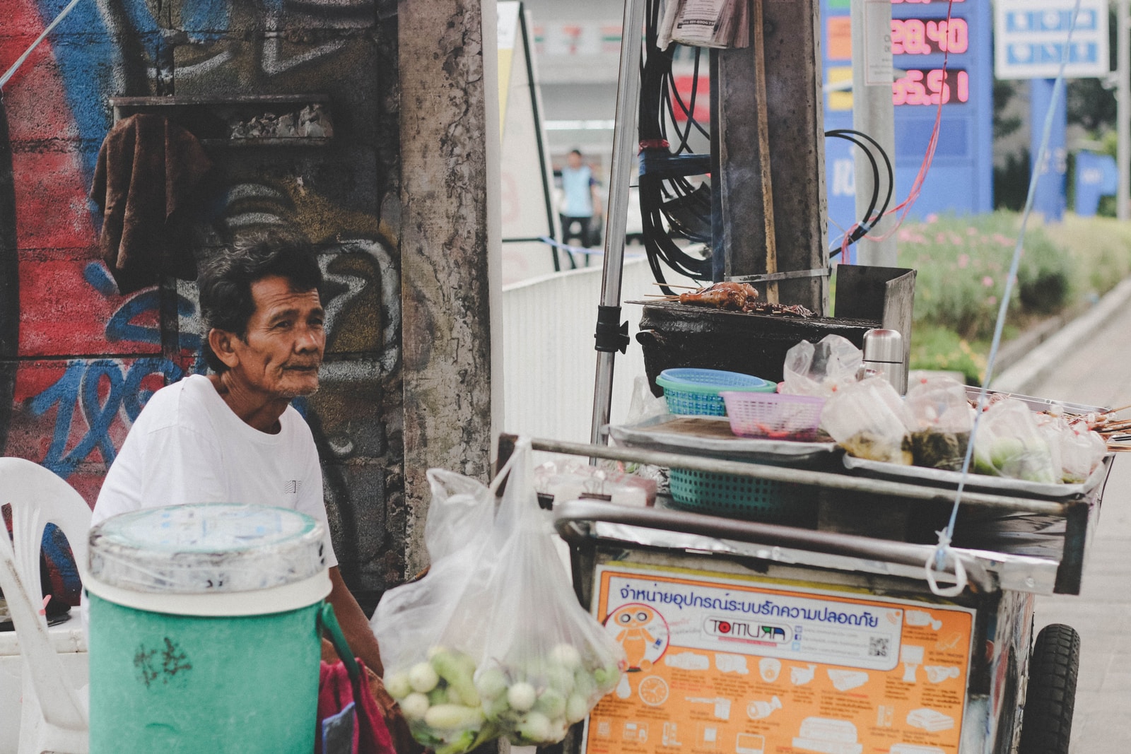 man in white top sitting in front of food stall