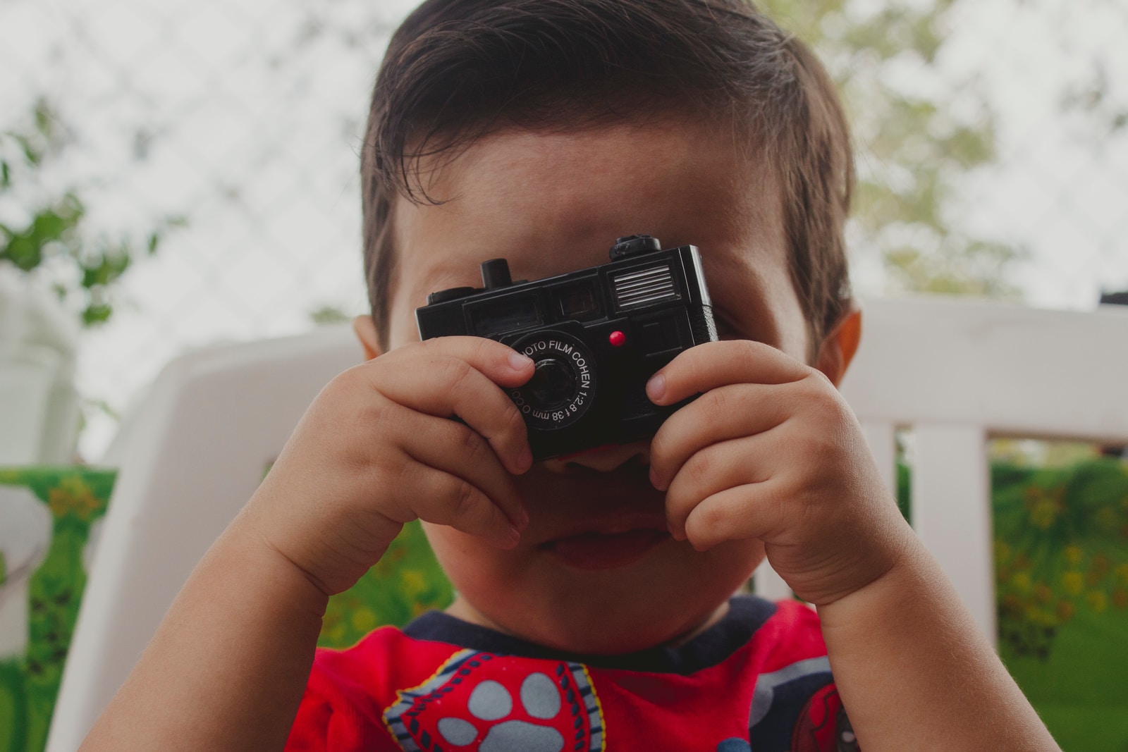 boy in red and blue crew neck t-shirt holding black dslr camera