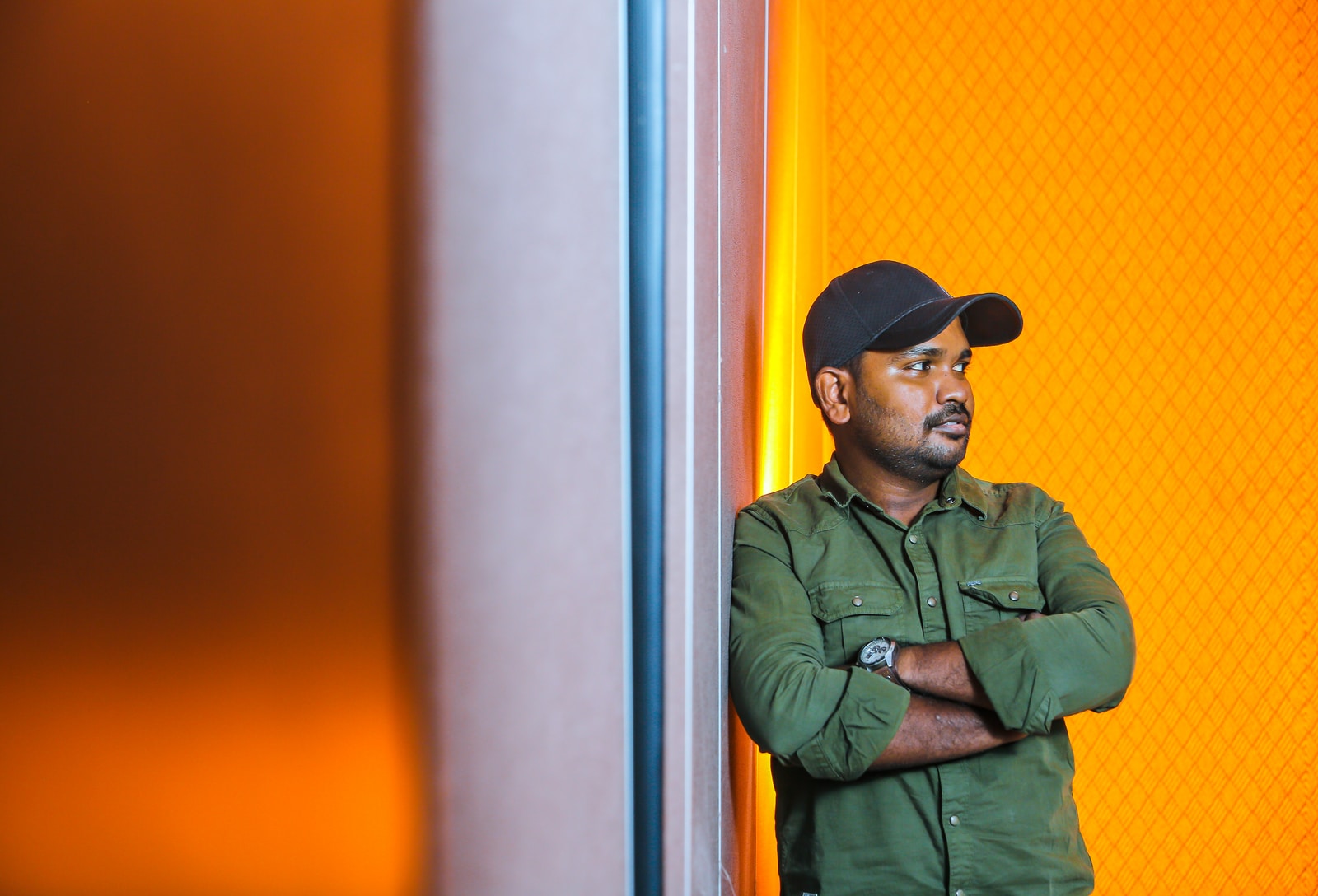 man in green button up shirt and black cap standing beside white wall