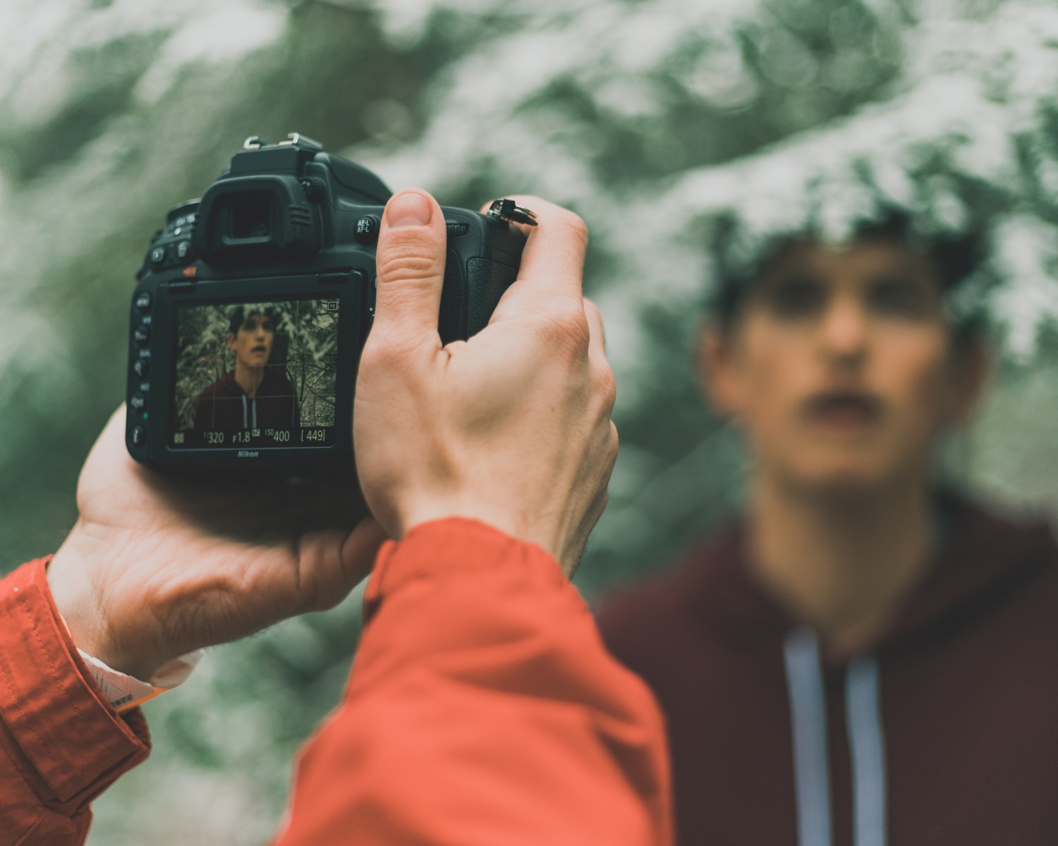 man in orange jacket holding black dslr camera