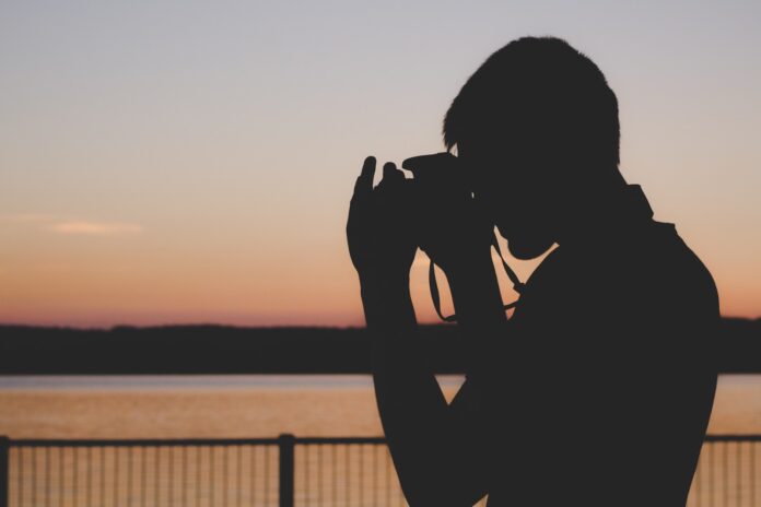 silhouette of man using camera near balustrade during sunset
