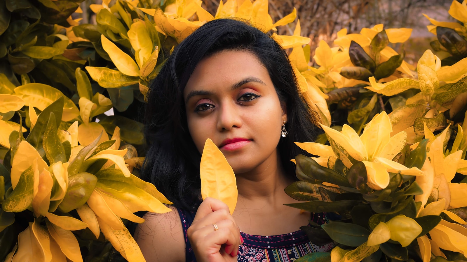 woman wearing multicolored floral boat-neck top standing in yellow leaf plant