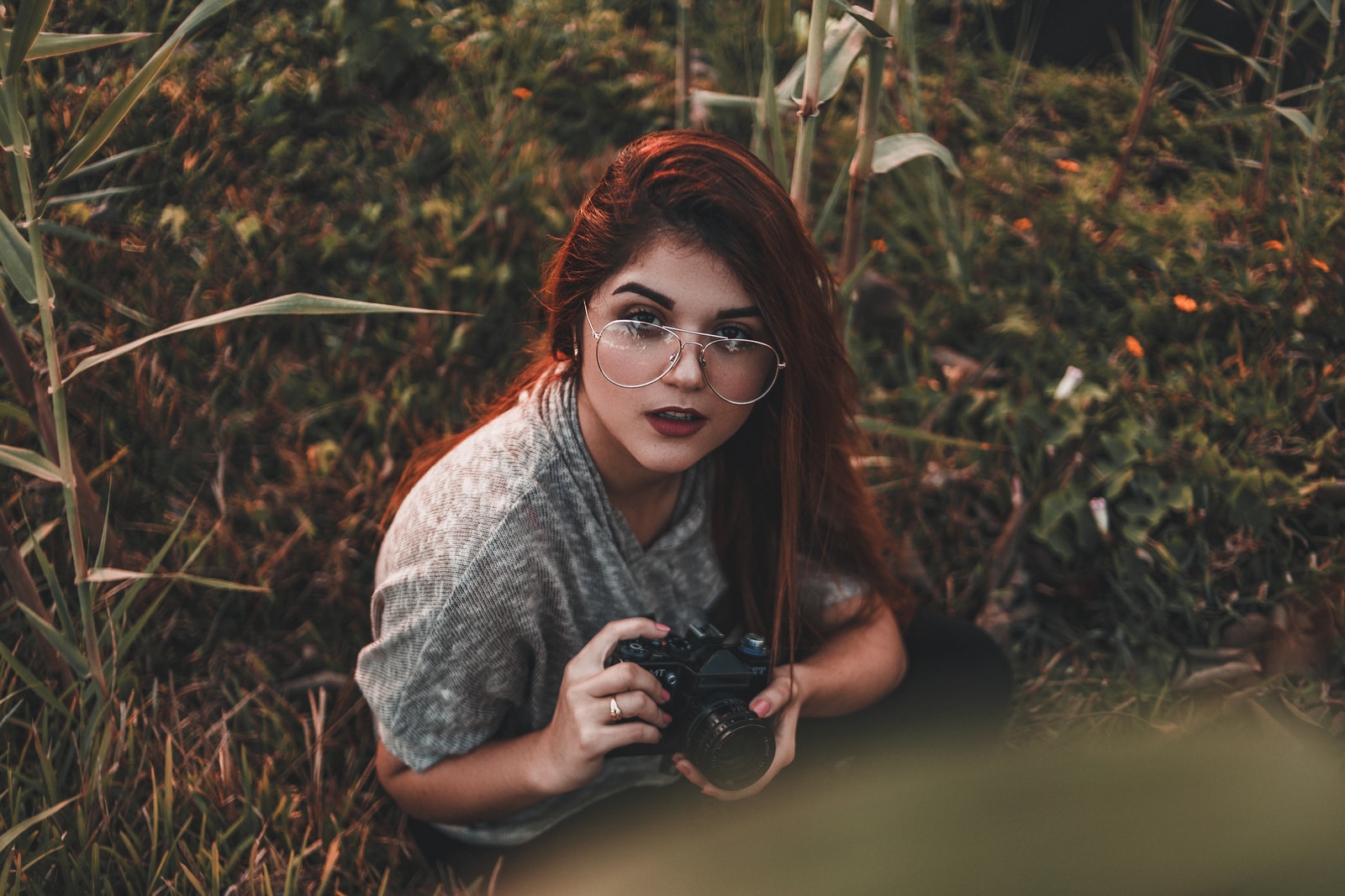 woman holding camera while sitting on grass