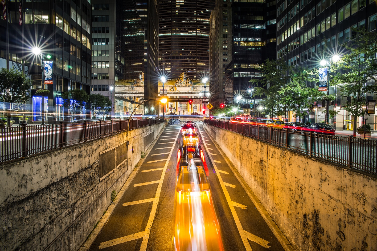 time lapse photography of vehicle passing on concrete road surround high-rise buildings during night time
