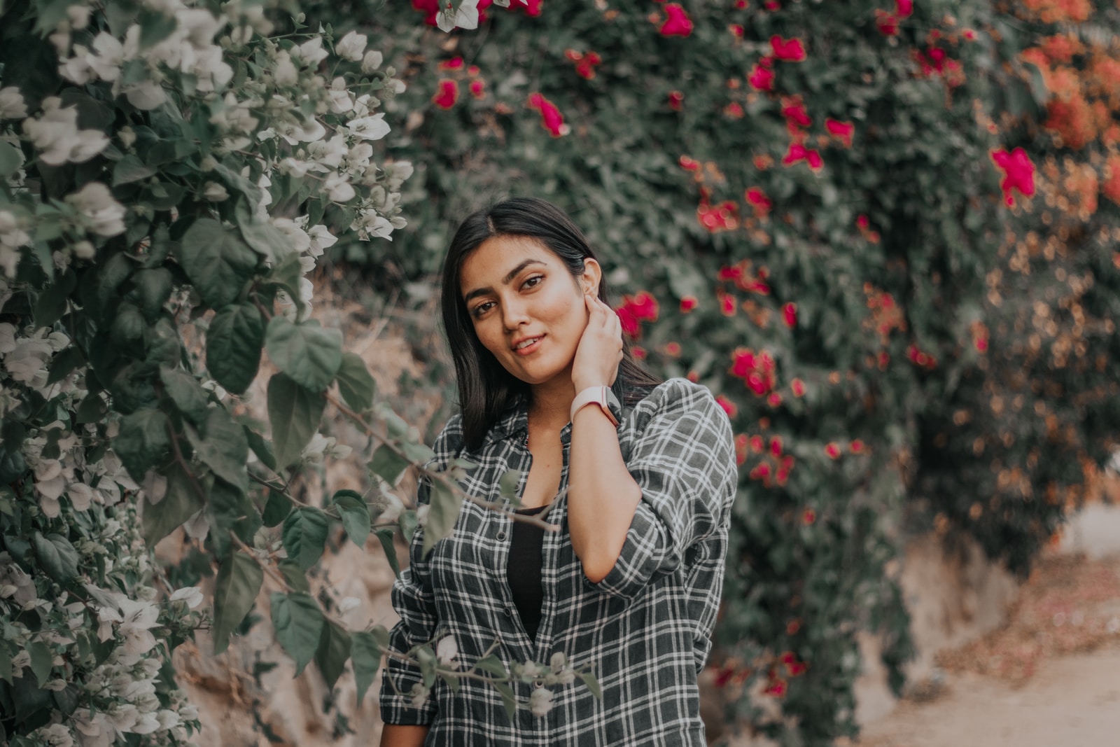 woman in black and white plaid dress shirt standing near red flowers