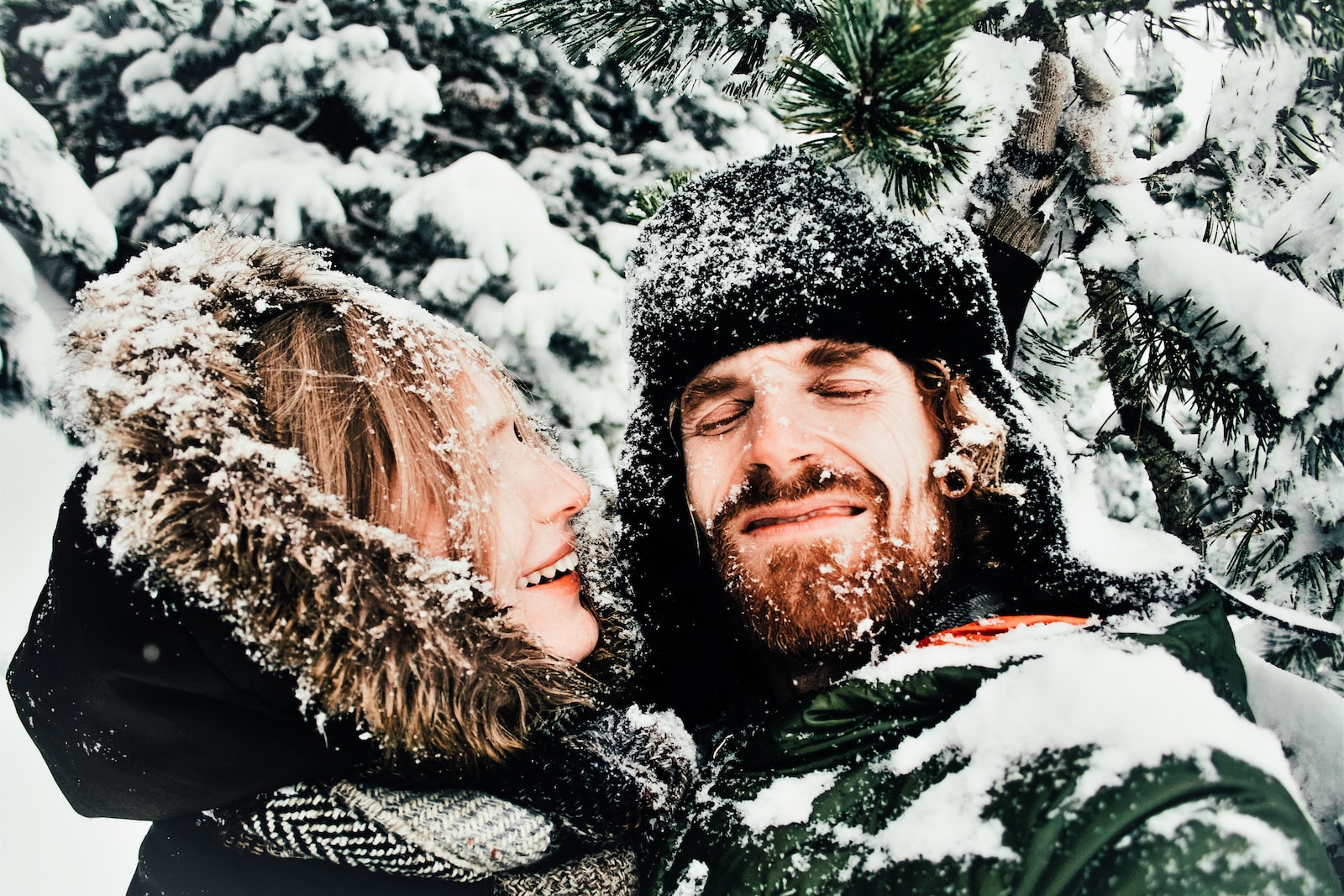 smiling man and woman standing under snow covered tree in winter