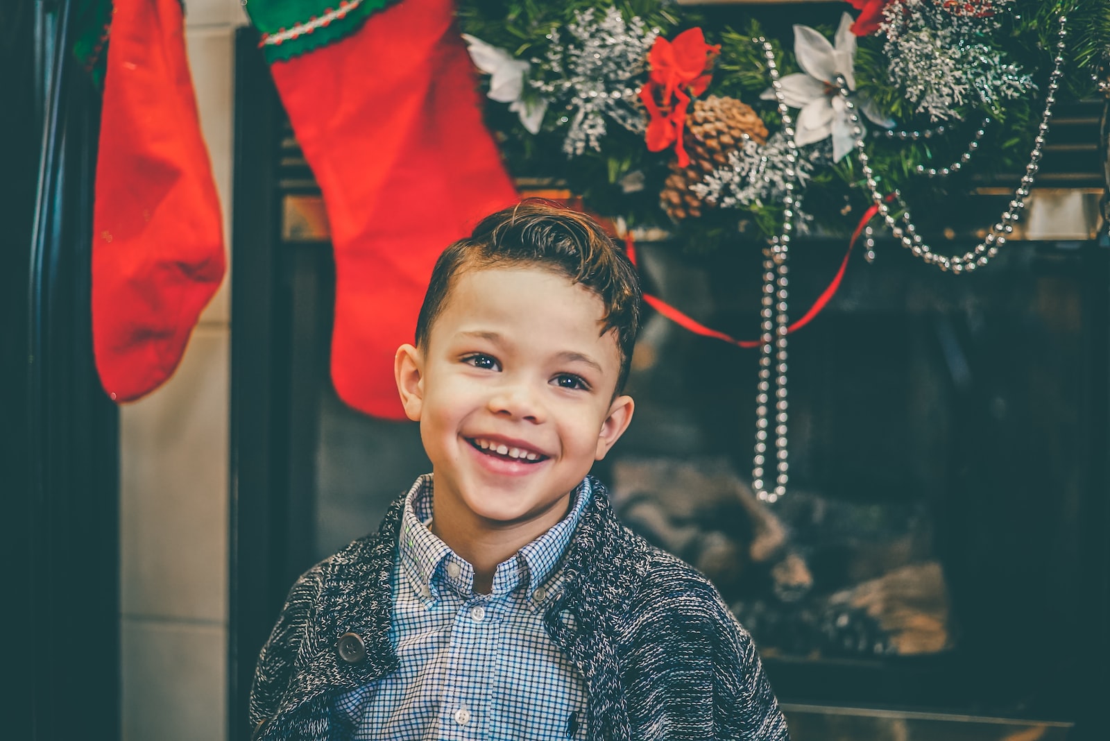 smiling boy in gray inner shirt and gray cardigan standing by fireplace with decors